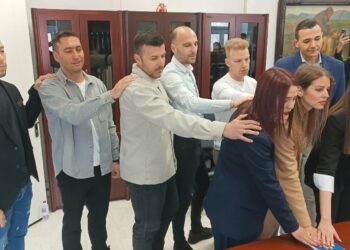 Εννέα νέοι δημοτικοί αστυνομικοί Φλώρινας ορκίζονται με το ένα χέρι υψωμένο, παρουσία συναδέλφων τους σε ένα γραφείο του Δημαρχείου.