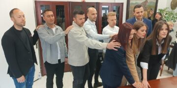 Εννέα νέοι δημοτικοί αστυνομικοί Φλώρινας ορκίζονται με το ένα χέρι υψωμένο, παρουσία συναδέλφων τους σε ένα γραφείο του Δημαρχείου.