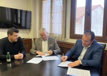 Τρεις άνδρες υπογράφουν ένα έγγραφο γύρω από ένα μεγάλο τραπέζι σε ένα γραφείο στο Αμύνταιο, στο πλαίσιο της ανακατασκευής των τουαλετών.