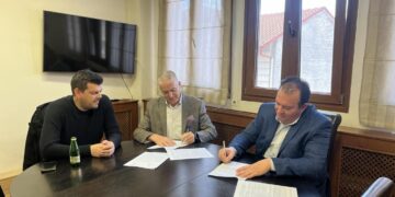 Τρεις άνδρες υπογράφουν ένα έγγραφο γύρω από ένα μεγάλο τραπέζι σε ένα γραφείο στο Αμύνταιο, στο πλαίσιο της ανακατασκευής των τουαλετών.