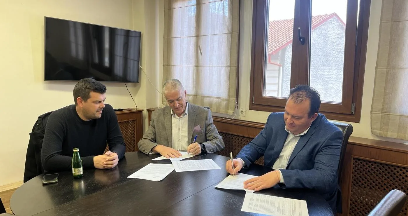 Τρεις άνδρες υπογράφουν ένα έγγραφο γύρω από ένα μεγάλο τραπέζι σε ένα γραφείο στο Αμύνταιο, στο πλαίσιο της ανακατασκευής των τουαλετών.