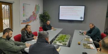 A group of people are seated around a large table in a meeting room discussing αντιπλημμυρικές εργασίες in the municipality of Florina.