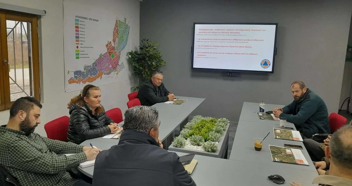 A group of people are seated around a large table in a meeting room discussing αντιπλημμυρικές εργασίες in the municipality of Florina.