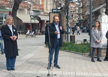 Ένας άνδρας με μικρόφωνο μιλάει στην πλατεία Γ. Μόδη στη Φλώρινα, ενώ γύρω του στέκονται άτομα, στο πλαίσιο της δασικής εκπαίδευσης Φλώρινας.