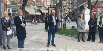 Ένας άνδρας με μικρόφωνο μιλάει στην πλατεία Γ. Μόδη στη Φλώρινα, ενώ γύρω του στέκονται άτομα, στο πλαίσιο της δασικής εκπαίδευσης Φλώρινας.