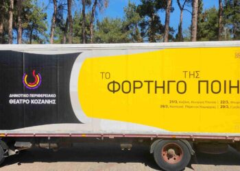 Ένα κόκκινο φορτηγό με την επιγραφή «Το Φορτηγό της Ποίησης» βρίσκεται σε ένα πάρκινγκ με δέντρα, προσφέροντας μια μοναδική θεατρική εμπειρία στην Καστοριά και τα Γρεβενά.