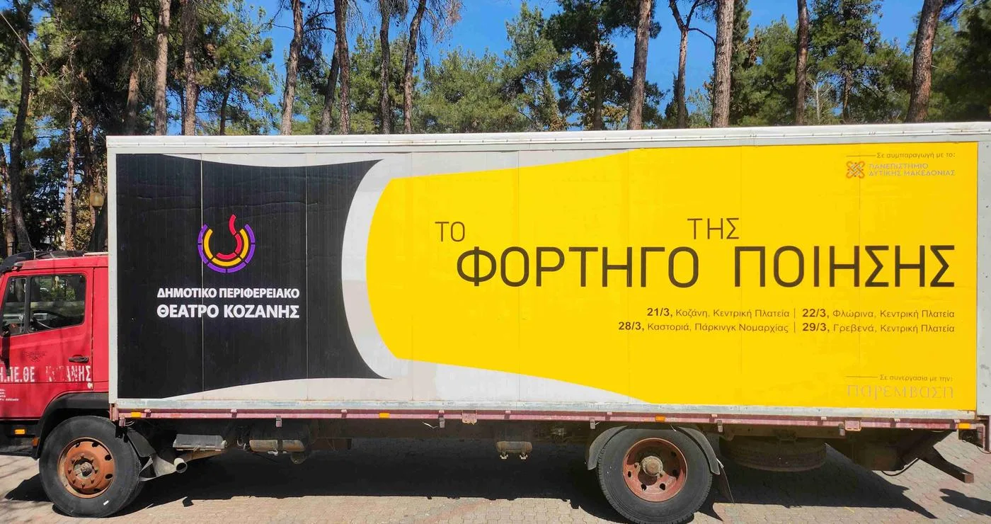 Ένα κόκκινο φορτηγό με την επιγραφή «Το Φορτηγό της Ποίησης» βρίσκεται σε ένα πάρκινγκ με δέντρα, προσφέροντας μια μοναδική θεατρική εμπειρία στην Καστοριά και τα Γρεβενά.