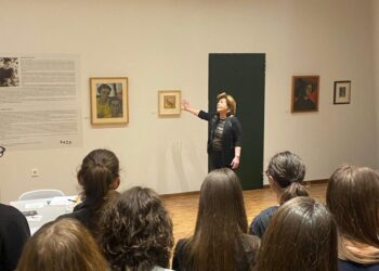 Μια ομάδα μαθητών παρακολουθεί τη Βάσω Κατράκη να εξηγεί τα έργα της στην έκθεση της Κοβεντάρειου Δημοτικής Βιβλιοθήκης στην Κοζάνη.