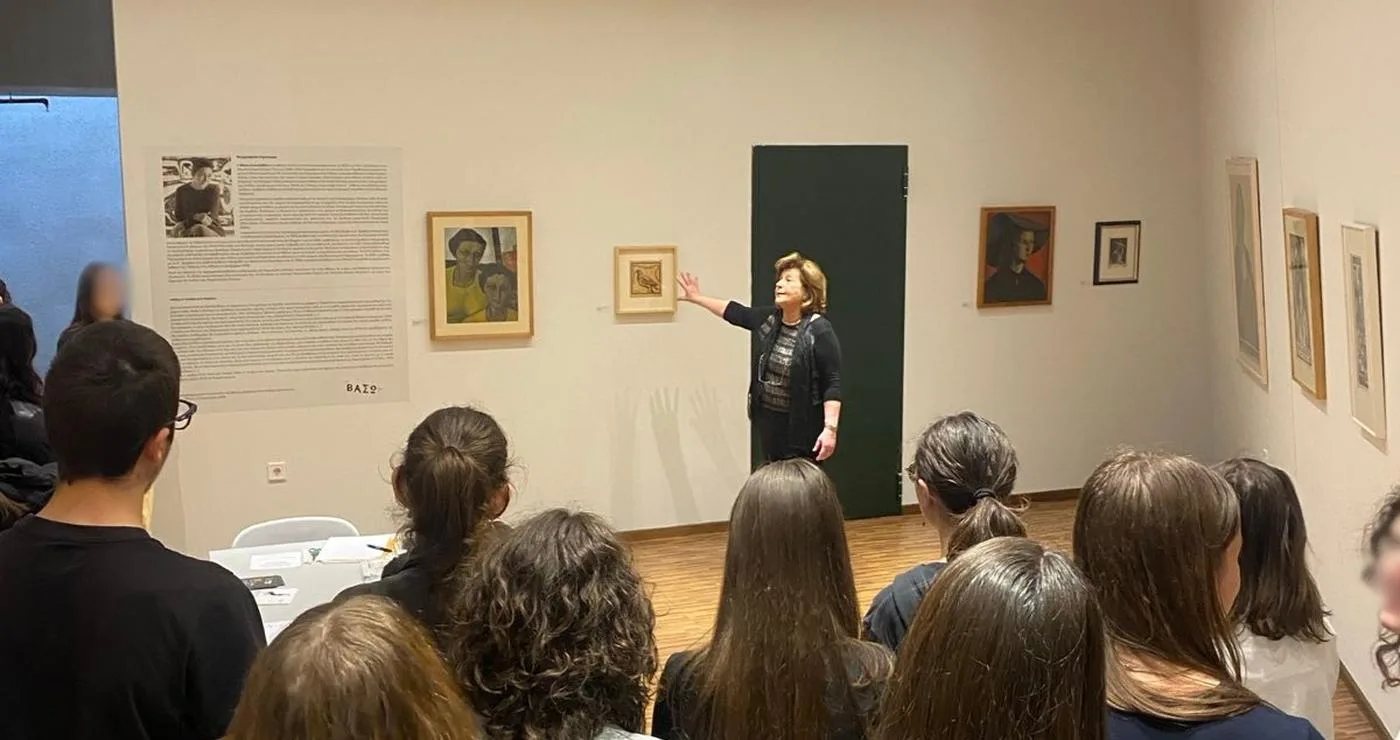 Μια ομάδα μαθητών παρακολουθεί τη Βάσω Κατράκη να εξηγεί τα έργα της στην έκθεση της Κοβεντάρειου Δημοτικής Βιβλιοθήκης στην Κοζάνη.