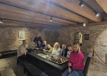 Μια ομάδα ανθρώπων κάθεται γύρω από ένα μεγάλο πέτρινο τραπέζι σε ένα κελάρι, στο πλαίσιο της συνάντησης του δήμου Πρεσπών για τον τουρισμό.