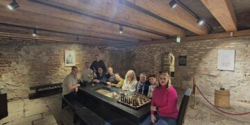 Μια ομάδα ανθρώπων κάθεται γύρω από ένα μεγάλο πέτρινο τραπέζι σε ένα κελάρι, στο πλαίσιο της συνάντησης του δήμου Πρεσπών για τον τουρισμό.