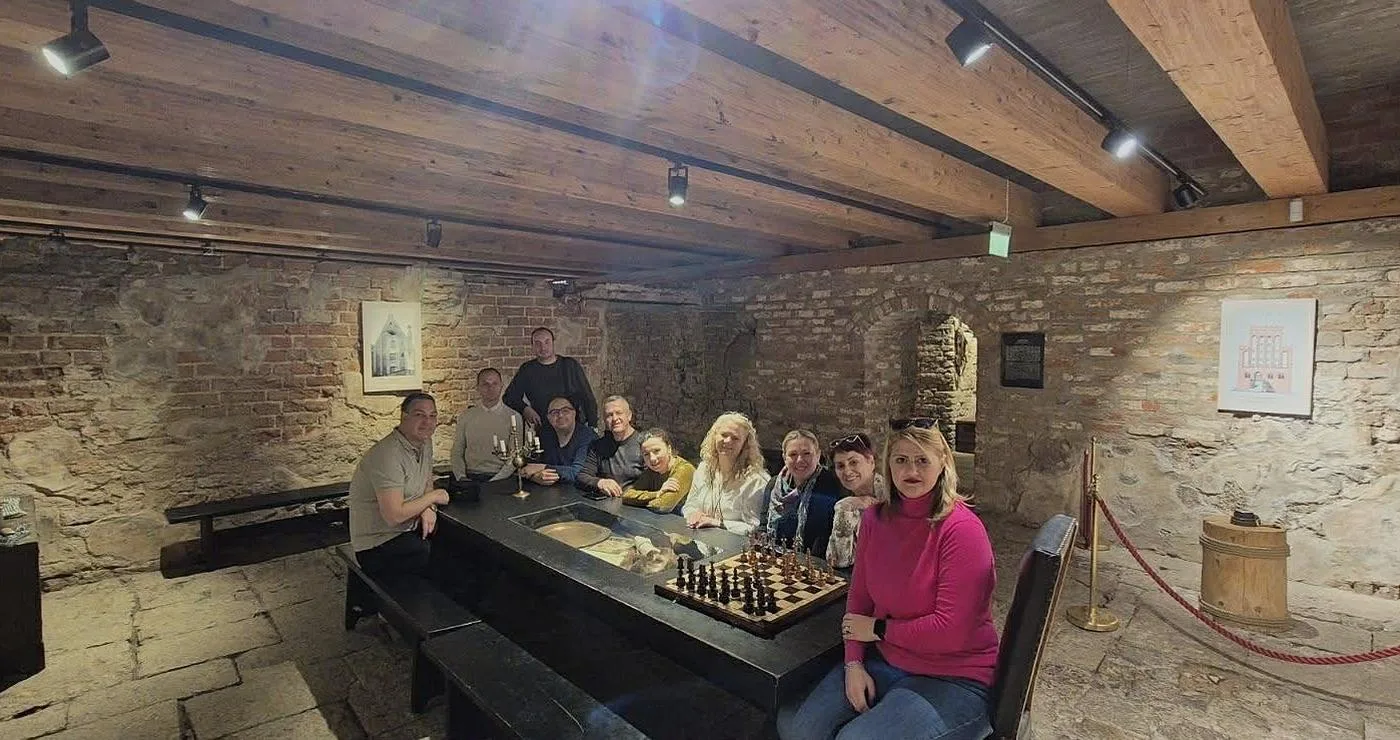 Μια ομάδα ανθρώπων κάθεται γύρω από ένα μεγάλο πέτρινο τραπέζι σε ένα κελάρι, στο πλαίσιο της συνάντησης του δήμου Πρεσπών για τον τουρισμό.