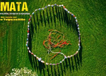 Άνθρωποι στέκονται σε έναν πράσινο αγρό, σχηματίζοντας έναν κύκλο και κρατώντας πολύχρωμα νήματα, συμβολίζοντας το ντοκιμαντέριο «Νήματα» στην Κοζάνη.