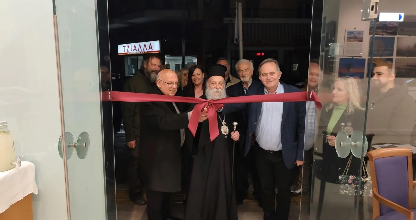 Στην έκθεση φωτογραφίας Γρεβενών, ο Μητροπολίτης Γρεβενών και ο Δήμαρχος κόβουν την κορδέλα στα εγκαίνια, με πλήθος κόσμου να παρακολουθεί.