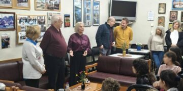 Μια ομάδα μαθητών και συνοδών κατά την επίσκεψη δημοτικού σχολείου στο ΚΑΠΗ Αμυνταίου, περιτριγυρισμένοι από φωτογραφίες και χαμογελαστοί.