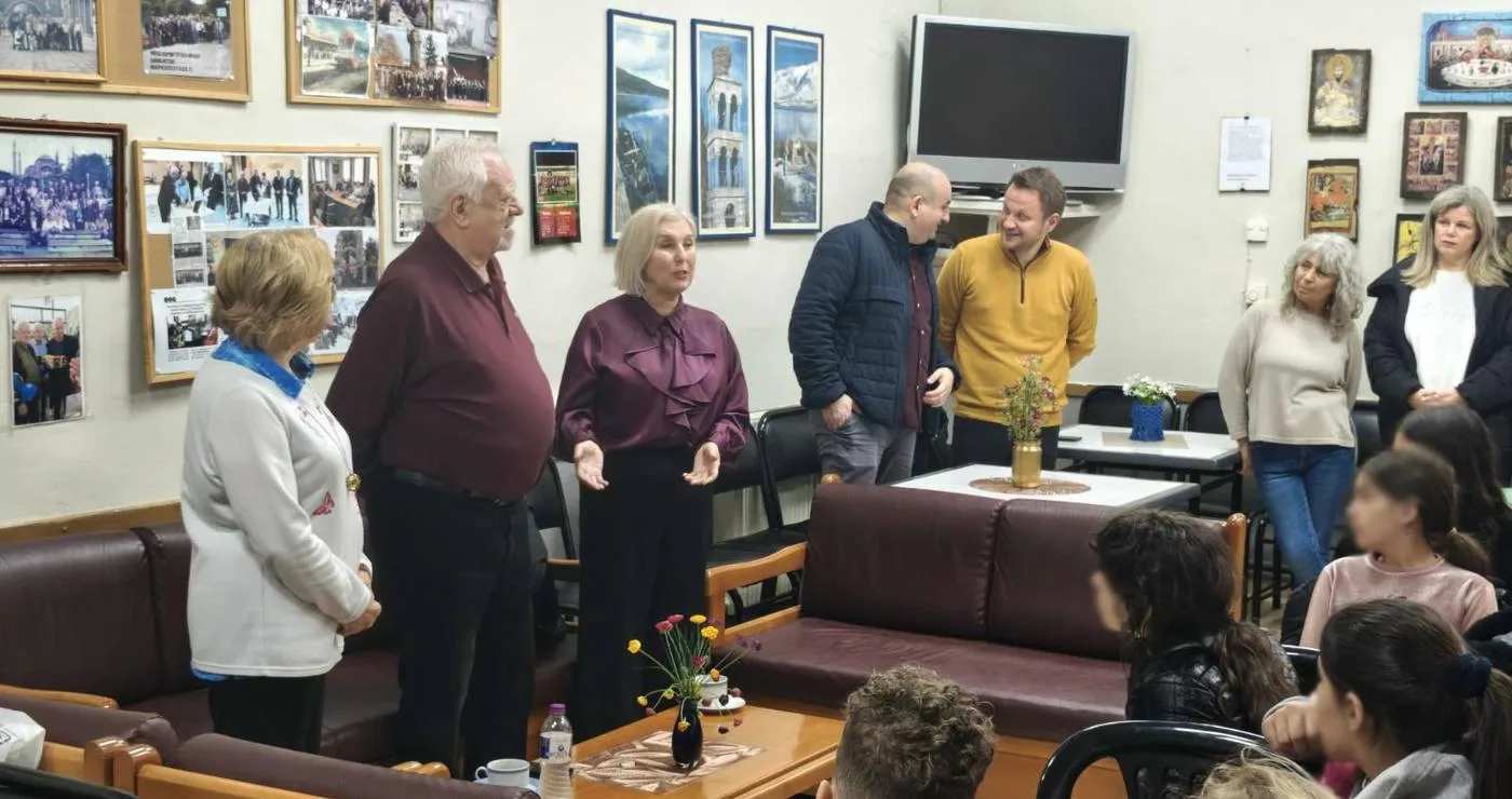 Μια ομάδα μαθητών και συνοδών κατά την επίσκεψη δημοτικού σχολείου στο ΚΑΠΗ Αμυνταίου, περιτριγυρισμένοι από φωτογραφίες και χαμογελαστοί.