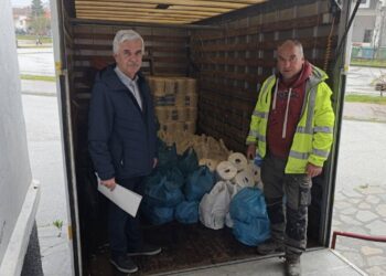 Δύο άνδρες στέκονται χαμογελαστοί μπροστά από ένα φορτηγό γεμάτο με πακέτα τροφίμων, στο πλαίσιο της διανομής τροφίμων στο Άργος Ορεστικό.