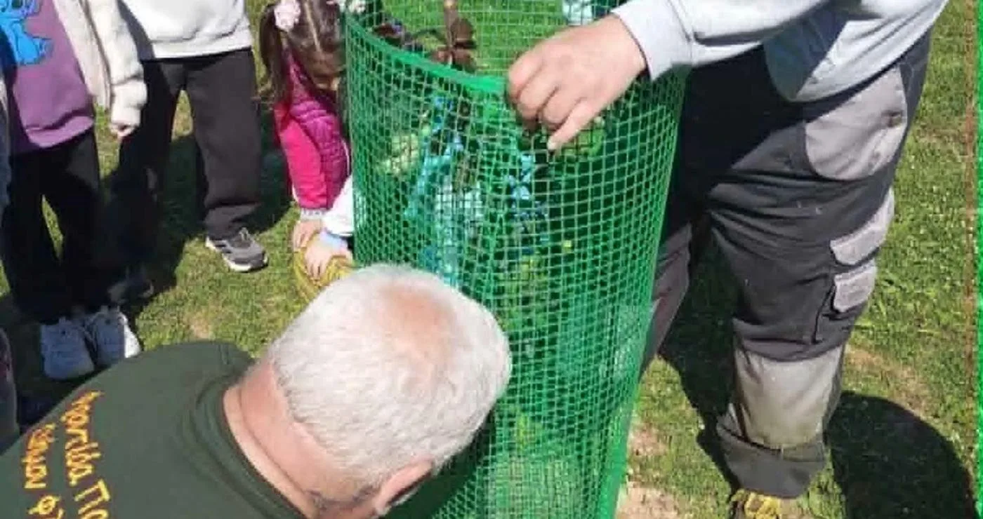 Ένας άνδρας με αναπηρία βοηθάει παιδιά να φυτέψουν ένα δενδρύλλιο στο 8ο Νηπιαγωγείο Φλώρινας κατά τη δράση Δεντροφύτευση Φλώρινα.