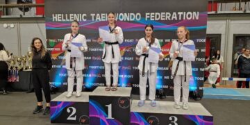 Τρεις αθλήτριες της Μακεδονικής Δύναμης Κοζάνης στέκονται στο βάθρο των νικητών στο Πανελλήνιο Κύπελλο Ταεκβοντό, φορώντας τις στολές τους και τα μετάλλιά τους.