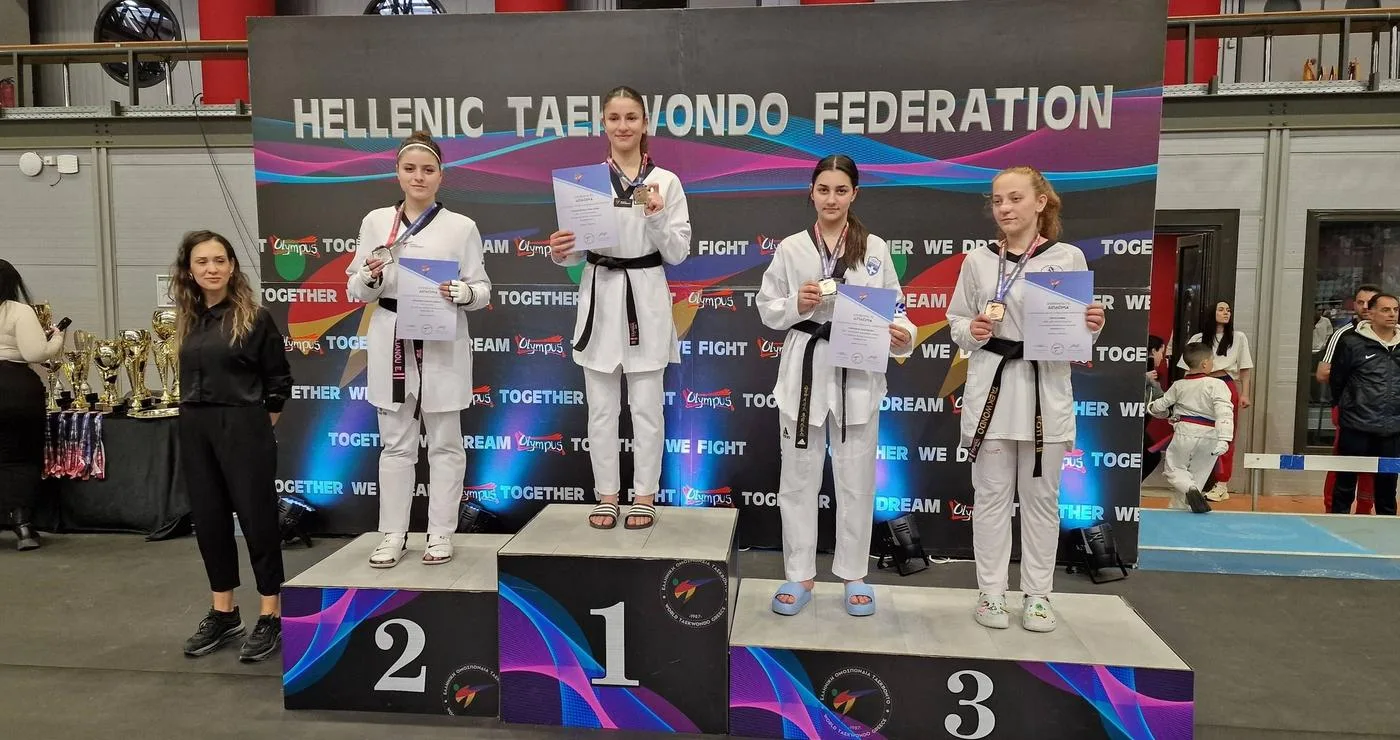 Τρεις αθλήτριες της Μακεδονικής Δύναμης Κοζάνης στέκονται στο βάθρο των νικητών στο Πανελλήνιο Κύπελλο Ταεκβοντό, φορώντας τις στολές τους και τα μετάλλιά τους.