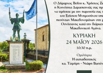 Ένα άγαλμα ενός Μακεδονομάχου στέκεται μπροστά από ένα μνημείο στο χωριό Δαμασκηνιά, ενώ γύρω του υπάρχουν σημαίες και ένα όμορφο τοπίο, τιμώντας το μνημόσυνο μακεδονομάχων.