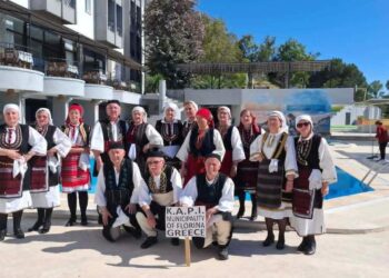 Μέλη της χορωδίας και του χορευτικού τμήματος του ΚΑΠΗ Φλώρινας, ντυμένα με παραδοσιακές στολές, ποζάρουν χαμογελαστοί μπροστά από ένα κτίριο κατά την διάρκεια της Γιορτής Φράουλας.