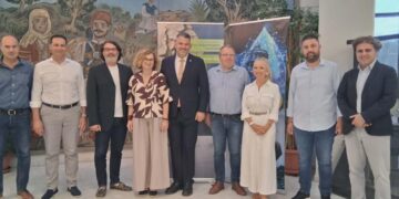 Μια ομάδα ανθρώπων στέκεται μπροστά από έναν τοίχο με μια τοιχογραφία, αντιπροσωπεύοντας τον δήμο Φλώρινας και τα ποτάμια της περιοχής.