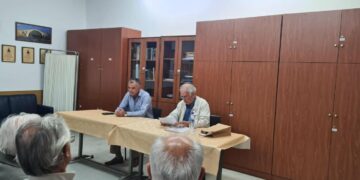 Ο ιστορικός Απόστολος Παπαδημητρίου παρουσιάζει την μάχη Σπηλαίου Γρεβενών σε ένα πλήθος ανθρώπων σε μια αίθουσα με ξύλινα ντουλάπια.