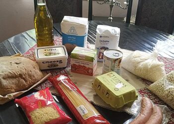 Τρόφιμα μακράς διάρκειας, όπως ζυμαρικά, λάδι και φασόλια, τοποθετούνται πάνω σε ένα ξύλινο τραπέζι σε ένα παραδοσιακό σαλόνι, μέρος των κοινωνικών δράσεων του Φιλοπρόοδου Συλλόγου Κοζάνης.