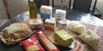 Τρόφιμα μακράς διάρκειας, όπως ζυμαρικά, λάδι και φασόλια, τοποθετούνται πάνω σε ένα ξύλινο τραπέζι σε ένα παραδοσιακό σαλόνι, μέρος των κοινωνικών δράσεων του Φιλοπρόοδου Συλλόγου Κοζάνης.