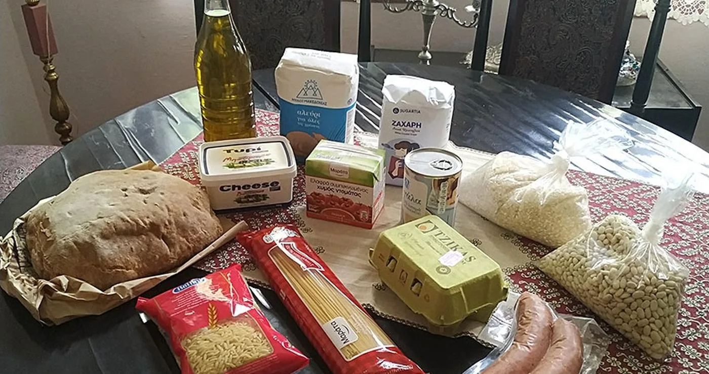 Τρόφιμα μακράς διάρκειας, όπως ζυμαρικά, λάδι και φασόλια, τοποθετούνται πάνω σε ένα ξύλινο τραπέζι σε ένα παραδοσιακό σαλόνι, μέρος των κοινωνικών δράσεων του Φιλοπρόοδου Συλλόγου Κοζάνης.