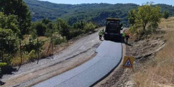 Η οδοποιία Βοΐου προχωράει, με μια νέα ασφαλτοστρωμένη οδική αρτηρία να διασχίζει ένα καταπράσινο τοπίο με λόφους και δέντρα.