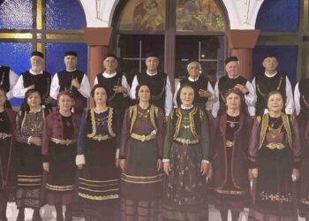 Μια ομάδα χορευτών και μελών του Συλλόγου Γρεβενιωτών Κοζάνης ποζάρουν φορώντας παραδοσιακές στολές μπροστά από ένα εκκλησάκι κατά τη διάρκεια των Γρεβενιώτικων εκδηλώσεων Κοζάνης.