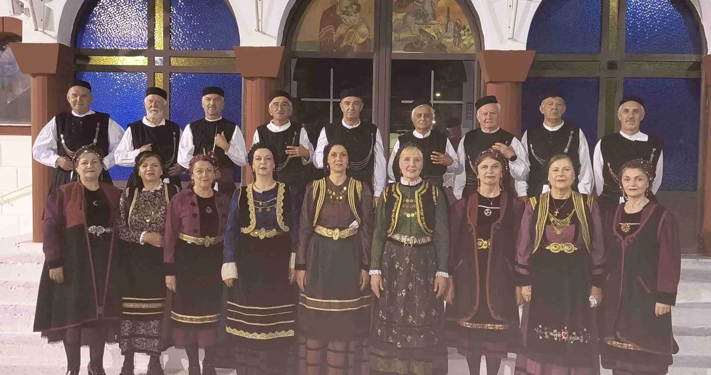 Μια ομάδα χορευτών και μελών του Συλλόγου Γρεβενιωτών Κοζάνης ποζάρουν φορώντας παραδοσιακές στολές μπροστά από ένα εκκλησάκι κατά τη διάρκεια των Γρεβενιώτικων εκδηλώσεων Κοζάνης.