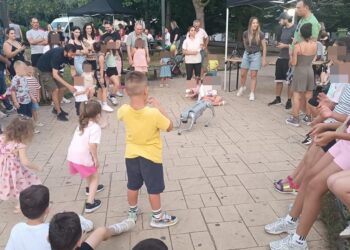 Μια ομάδα παιδιά συμμετέχει με ενθουσιασμό στο παιδικό φεστιβάλ Φλώρινας, χορεύοντας σε έναν κυκλικό χώρο στο Νέο Πάρκο.