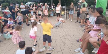 Μια ομάδα παιδιά συμμετέχει με ενθουσιασμό στο παιδικό φεστιβάλ Φλώρινας, χορεύοντας σε έναν κυκλικό χώρο στο Νέο Πάρκο.