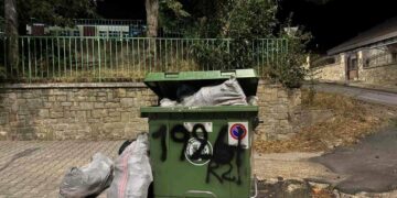 Ένας πράσινος μεταλλικός κάδος για οικοδομικά απόβλητα, γεμάτος με μπάζα και τσουβάλια, βρίσκεται σε έναν δρόμο με λιθόστρωτο στην Φλώρινα.
