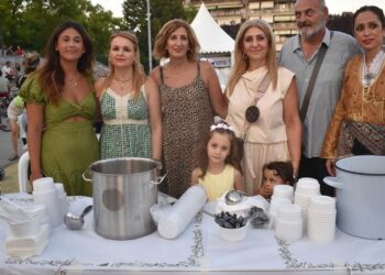 Μια ομάδα ανθρώπων στέκεται πίσω από έναν πάγκο με ποτήρια και κατσαρόλες, προσφέροντας Πατρίδων Γεύσεις σε μια εκδήλωση στο Νέο Πάρκο της Φλώρινας.