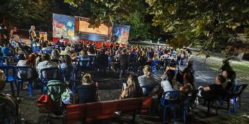 Ένα πλήθος θεατών παρακολουθεί με ενθουσιασμό μια παράσταση Θεάτρου Σκιών Λεβαία σε μια καλοκαιρινή βραδιά.