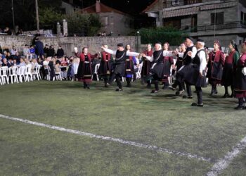 Μια ομάδα χορευτών από τους Γρεβενιώτες Κοζάνης χορεύουν σε ένα γήπεδο στην Κλεισούρα, με θεατές να παρακολουθούν το παραδοσιακό γλέντι.
