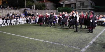 Μια ομάδα χορευτών από τους Γρεβενιώτες Κοζάνης χορεύουν σε ένα γήπεδο στην Κλεισούρα, με θεατές να παρακολουθούν το παραδοσιακό γλέντι.