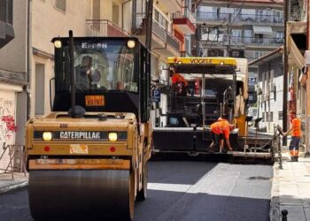 Μια μεγάλη πορτοκαλί κύλινδρος συμπιέζει την καινούργια άσφαλτο σε έναν κεντρικό δρόμο της Φλώρινας, στο πλαίσιο των ασφαλτοστρώσεων.
