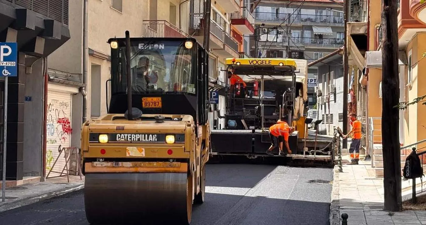 Μια μεγάλη πορτοκαλί κύλινδρος συμπιέζει την καινούργια άσφαλτο σε έναν κεντρικό δρόμο της Φλώρινας, στο πλαίσιο των ασφαλτοστρώσεων.