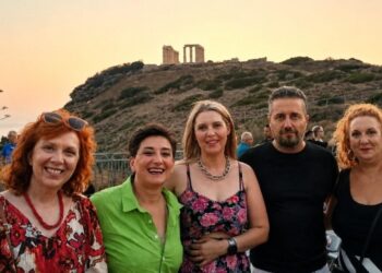 A group of five people smile for the camera with the Temple of Poseidon in Sounion visible in the background during the Κοζάνης - Λαυρεωτικής twinning event.