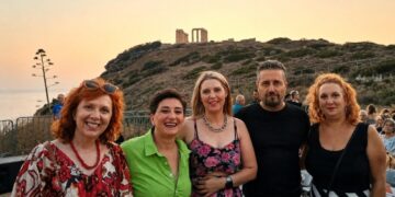 A group of five people smile for the camera with the Temple of Poseidon in Sounion visible in the background during the Κοζάνης - Λαυρεωτικής twinning event.