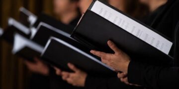 Μέλη χορωδίας κρατούν παρτιτούρες κατά τη διάρκεια της πρόβας, συμμετέχοντας στις χορωδίες του Δήμου Βοΐου.