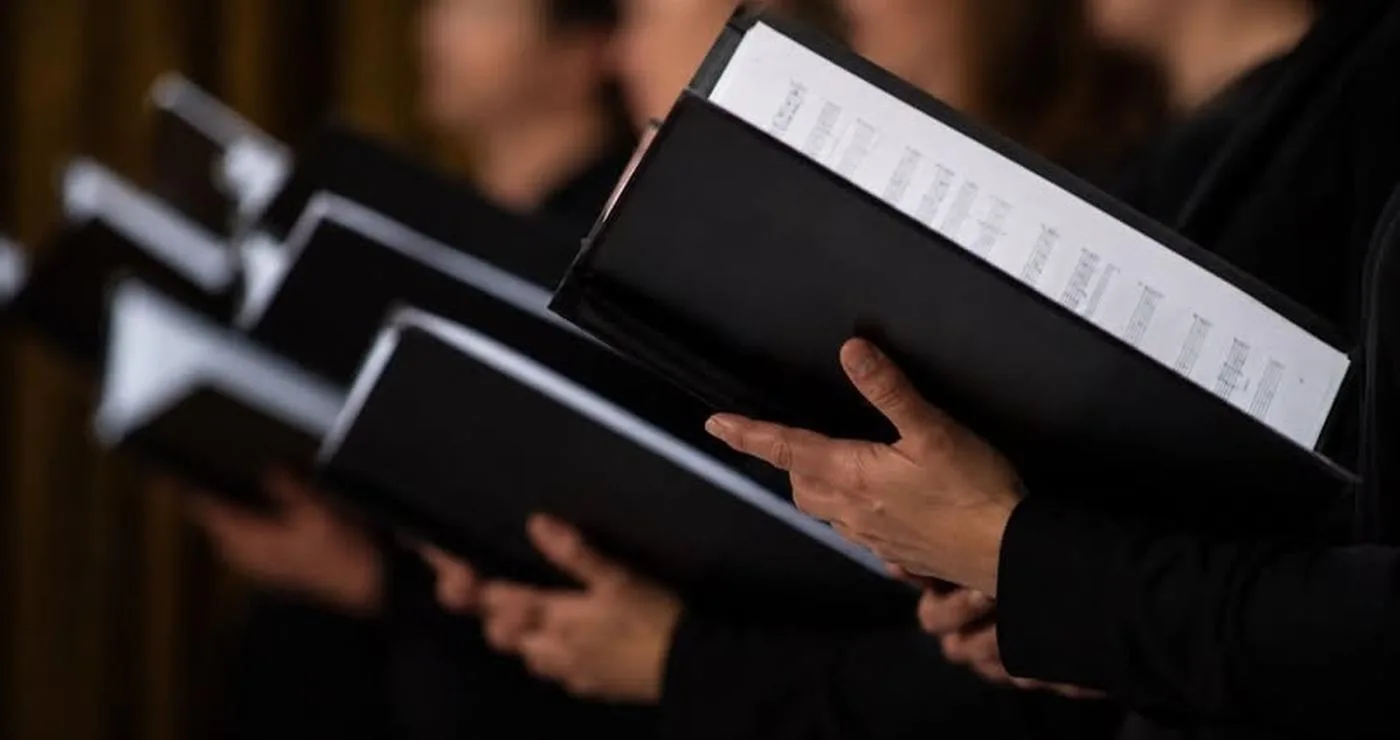 Μέλη χορωδίας κρατούν παρτιτούρες κατά τη διάρκεια της πρόβας, συμμετέχοντας στις χορωδίες του Δήμου Βοΐου.