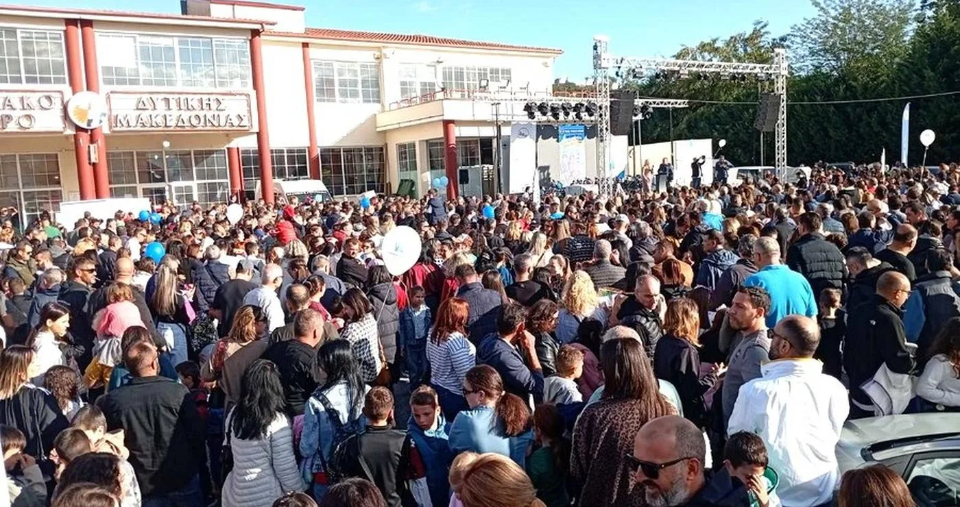 A large crowd of people gathers in front of the building hosting the Εμποροβιοτεχνική Έκθεση Δυτικής Μακεδονίας.