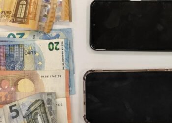 Ευρωπαϊκά χαρτονομίσματα των 5, 10, 20, 50 και 100 ευρώ τοποθετούνται πάνω σε ένα ξύλινο τραπέζι δίπλα σε τρία σπασμένα κινητά τηλέφωνα, ως μέρος των τηλεφωνικών απάτων στα Γρεβενά.