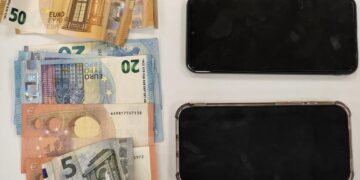 Ευρωπαϊκά χαρτονομίσματα των 5, 10, 20, 50 και 100 ευρώ τοποθετούνται πάνω σε ένα ξύλινο τραπέζι δίπλα σε τρία σπασμένα κινητά τηλέφωνα, ως μέρος των τηλεφωνικών απάτων στα Γρεβενά.
